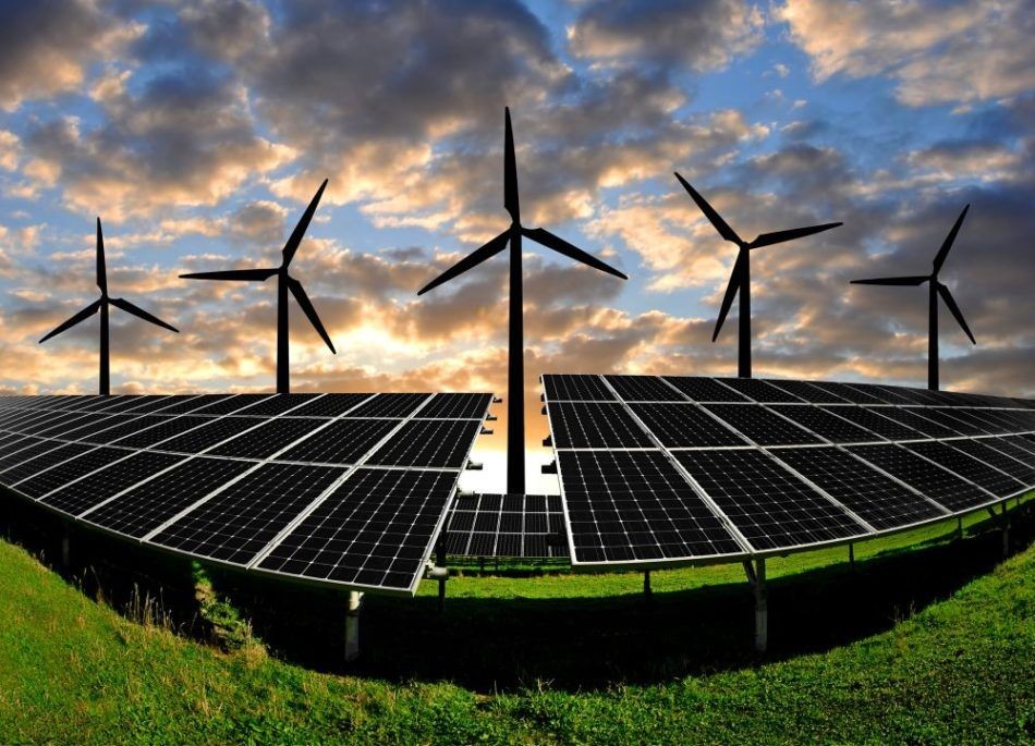 Solar panels and wind turbines on a grassy hill under a cloudy sky at sunset.